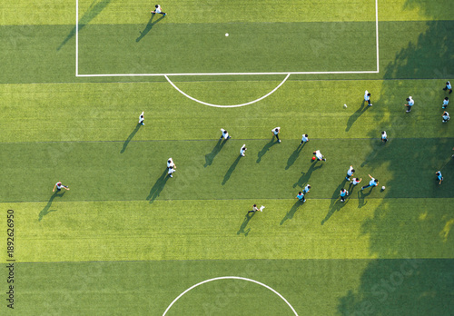 Aerial view of students playing soccer on a green campus field. Promoting physical education and teamwork during break time. Vibrant school sports scene.