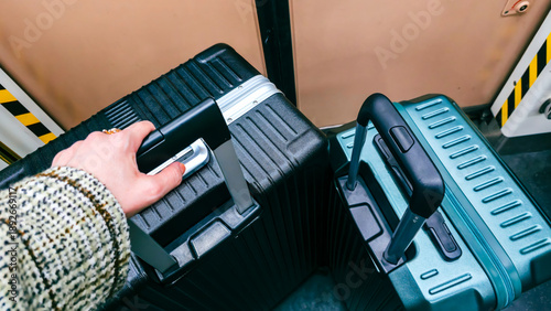POV of traveler holding black suitcase handle inside train next to teal luggage