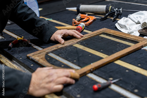 Foto Miroitier professionnel remplaçant les verres d’une très vieille pendule au bois fortement abîmé, mettant en valeur un travail de restauration artisanale sur un objet patrimonial