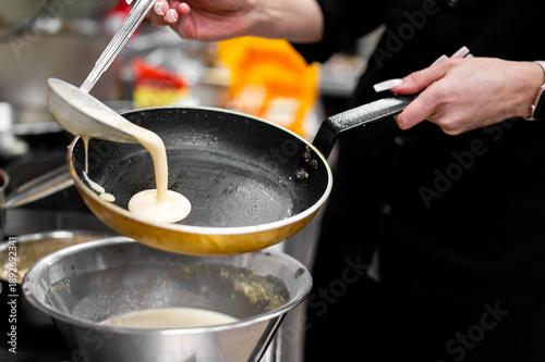 Schilderij op canvas Hands pouring liquid batter into a hot frying pan to cook a thin pancake or crep