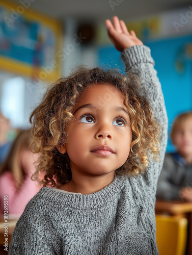 Candid educational lifestyle scene of a curious child raising a hand during a lesson in a classroom