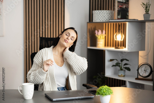 Quadro em tela A woman gently stretches her neck in a stylish office chair, promoting relaxation and comfort amid work