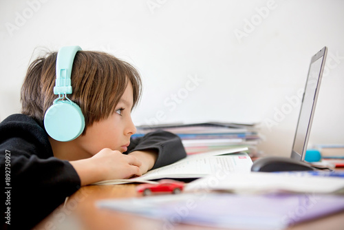 Foto Sad school child, struggling with studying, sitting at the table with laptop, wr