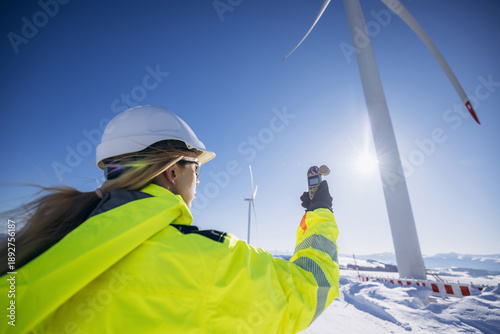 Fotografie Female engineer standing in large field energy windmills and using meteorological station to measure the wind speed