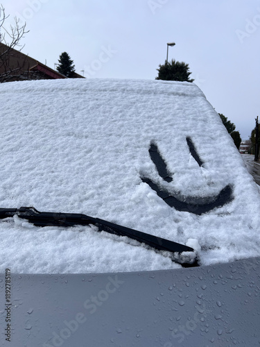 Coche cubierto de nieve recién caída, con textura, copiosa, vidrio delantero, luna, limpiaparabrisas, con una  carita feliz dibujada en la nieve, sonrisa, espacio copy