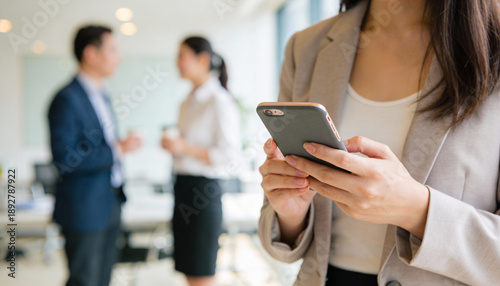 Businesswoman texting on smartphone in modern office corridor with colleagues