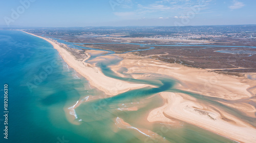 This aerial view shows Ria Formosa and Praia de Faro in Portugal, highlighting the coastline, waterways, and sandy beach under clear skies