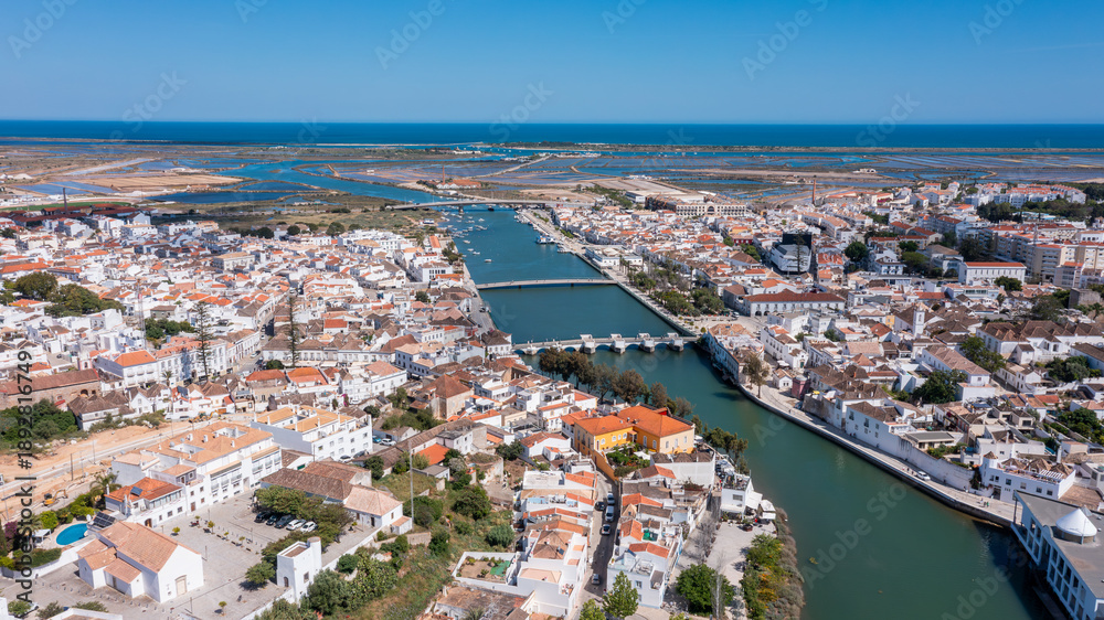 Fototapeta premium A drone view captures Tavira in Algarve with rivers, Roman bridges, and various structures. The coastline and landscapes are visible in the background