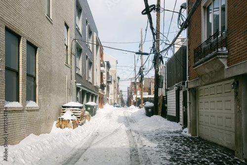 Billede på lærred Snow covers a city alley with buildings and power lines on a winter day in a bus