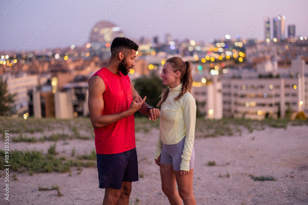 Fototapeta premium Couple discussing fitness data on smartwatch during evening workout