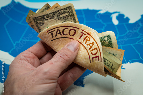 Hand holding a taco shell labeled TACO TRADE. Wall Street slang for a pattern where investors buy assets after President threatens tariffs, expecting him to back down and markets to rebound