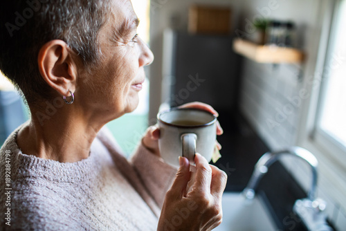 Bilde på lerret Senior woman sipping tea at home kitchen window