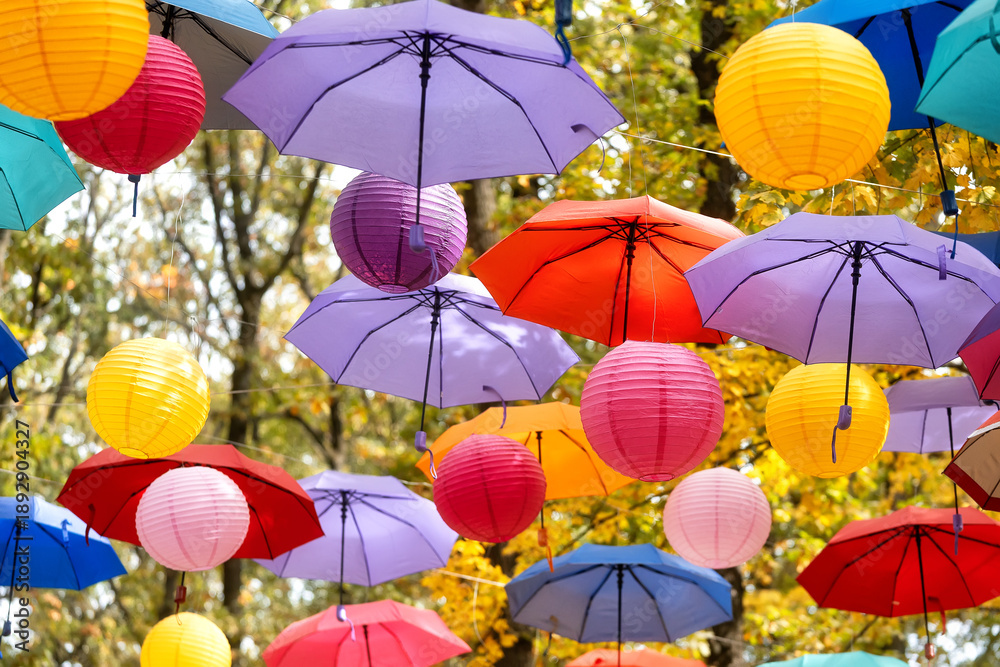Obraz premium Colorful umbrellas and paper lanterns hang overhead in autumn trees, creating a whimsical outdoor festival atmosphere full of joy everywhere.