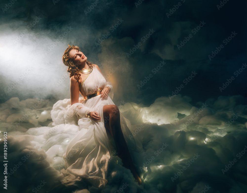 Obraz premium art photo real person fashion model, fantasy beauty woman goddess sitting in divine white soft clouds night sky magic rays light. Blonde curly hair angel girl in greek style dress golden laurel wreath