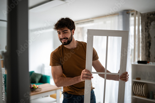 Tableau sur toile Young man smiling, holding window frame, home improvement