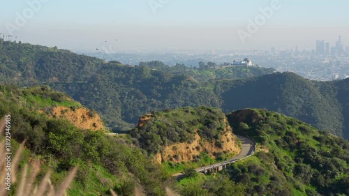 Panoramic view of the Los Angeles cityscape from the Hollywood Hills. Features the iconic Griffith Observatory with the downtown skyline in the hazy background.