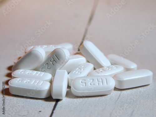 Foto White Medication Pills on Wooden Surface - Pile of white oval medication pills, some with  embossed, on a light textured wooden surface