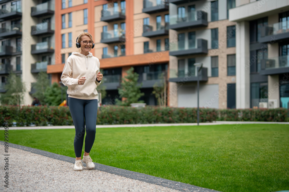 Fototapeta premium Mature woman jogging with headphones in urban park