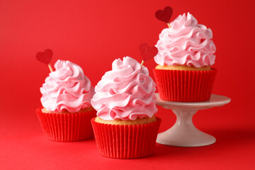 Happy Valentine's Day. Tasty cupcakes with heart toppers on red background, closeup