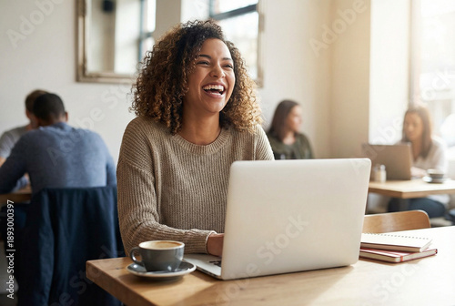 A woman is happily working at a cafe, smiling in front of a laptop with a cup of coffee