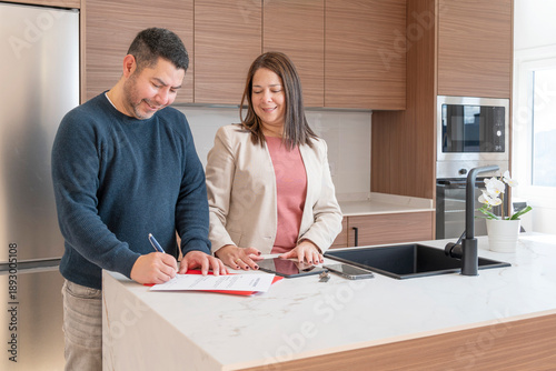 Man signing document with a female real estate agent in a modern kitchen