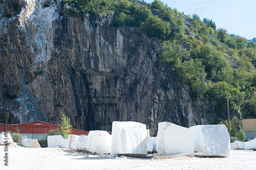 White marble blocks in stone quarry with rocky cliff and trees, industrial mining and raw material extraction