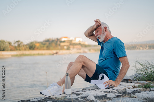 Fotografie Senior man wiping sweat after exercising by the river
