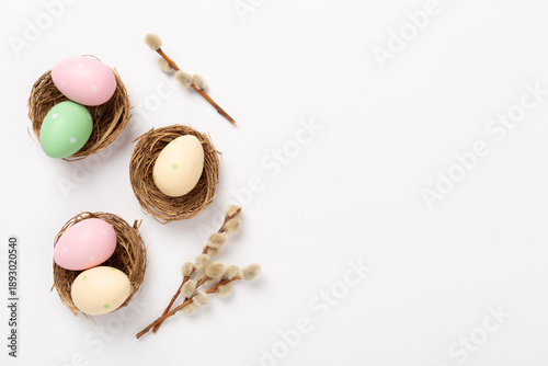 Colorful easter eggs in nests with flowers on color background, top view