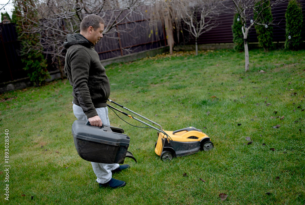 Fototapeta premium A lawn mower man mows the grass in the backyard. Agricultural machinery for garden maintenance.