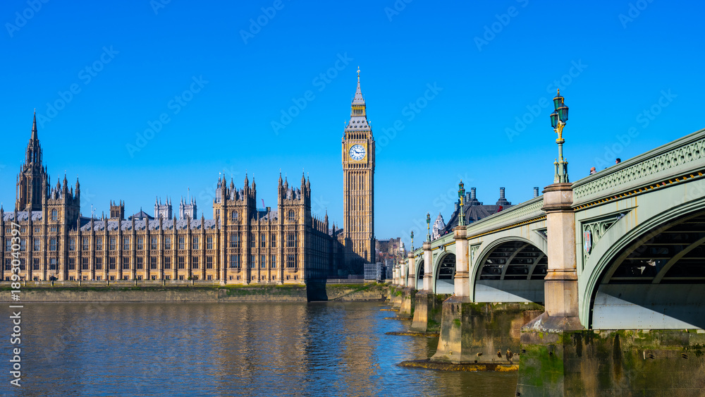Fototapeta premium The Houses of Parliament and Big Ben above the River Thames in London. The sky is clear and the iconic landmarks stand tall and proud.