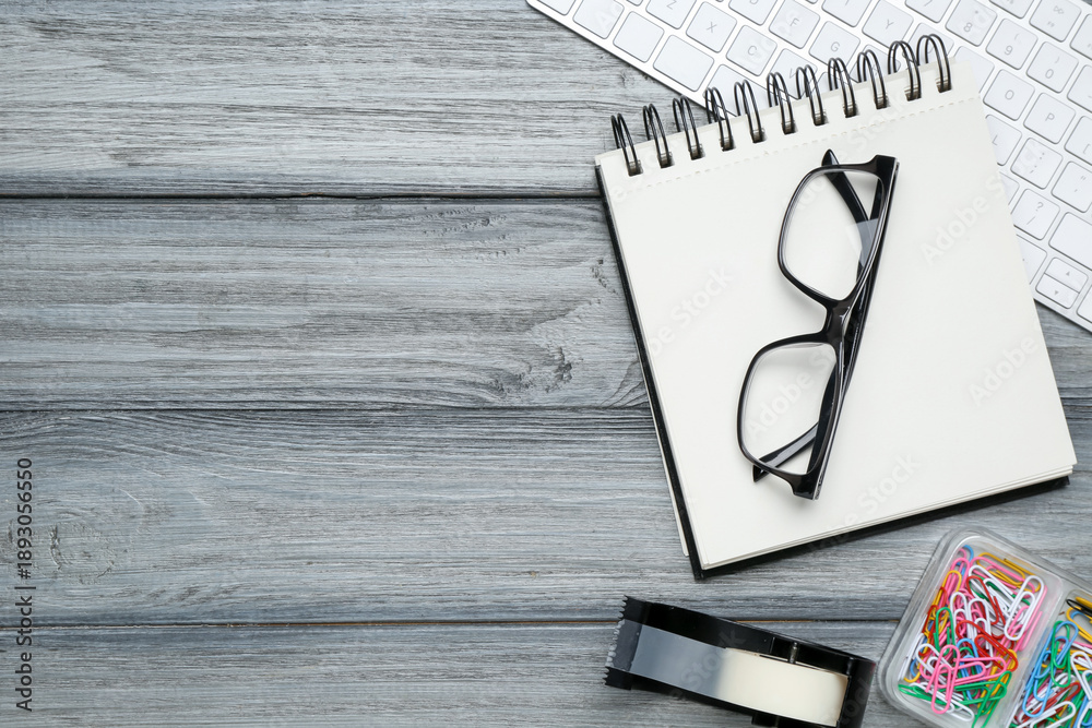 Fototapeta premium Office workplace. Computer keyboard, glasses and stationery on grey wooden desk, flat lay. Space for text