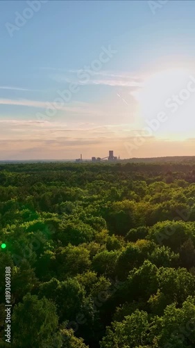 Aerial Drone Flight Over Forest Towards Industrial Factory Complex During Golden Sunset