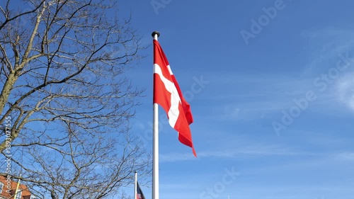 A view from below of a large Danish flag against a blue sky. Flag Day. Slow motion.