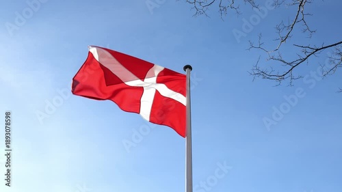 A view from below of a large Danish flag against a blue sky. Flag Day. Slow motion.