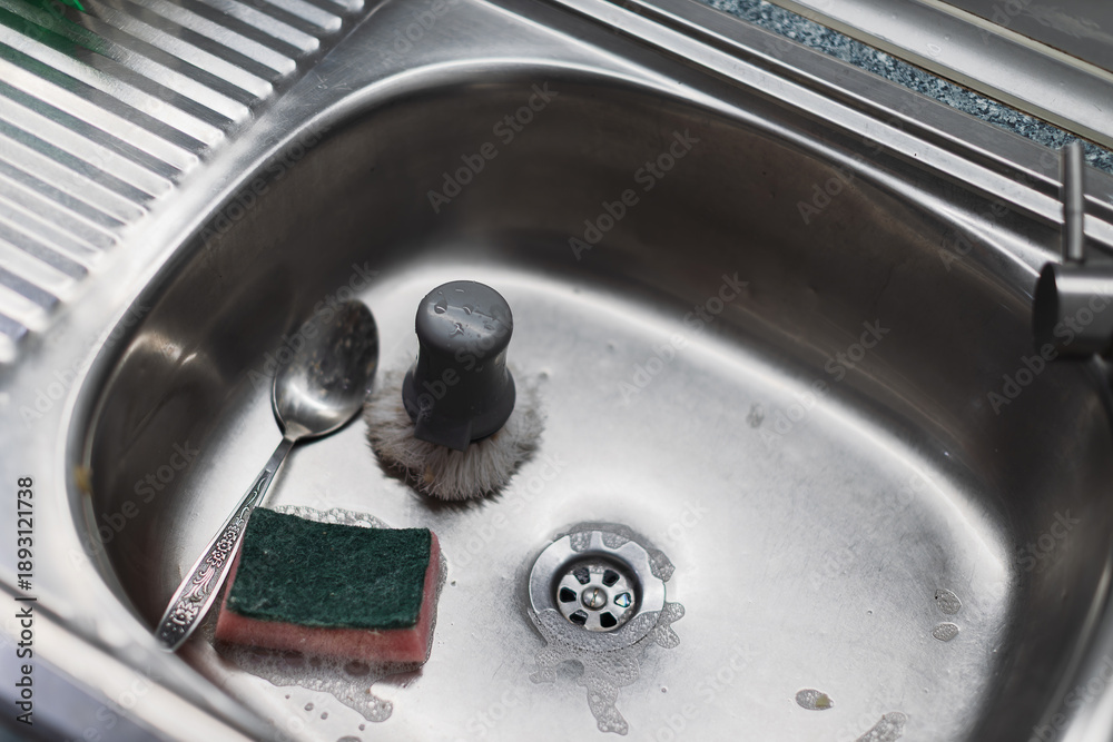 Obraz premium A kitchen sink with a sponge, spoon, and brush.