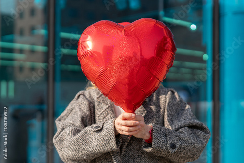Foto Holding a red heart balloon in front of a glass building on a sunny day with a p