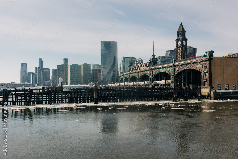 Obraz premium City skyline over calm water with pier and clock tower in the foreground during a sunny day