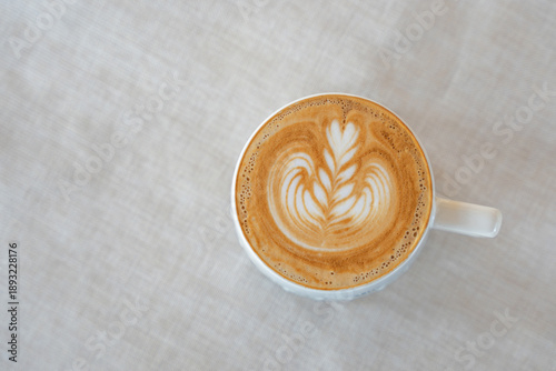 Top view hot coffee latte art flower shape in ceramic cup on cream colored fabric background. Copy space.