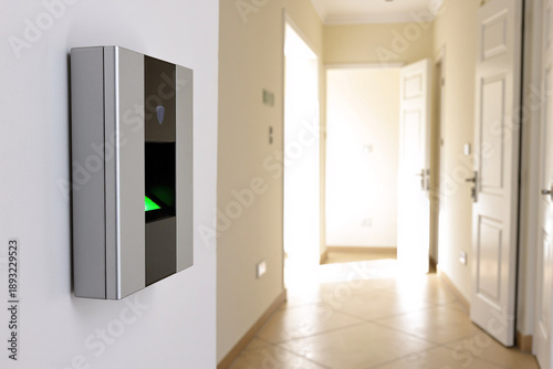 Modern silver biometric fingerprint scanner device mounted on a white wall in a residential home hallway for smart security and access control protection