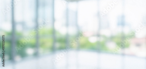 A blurred view through large glass windows showcases a vibrant cityscape with greenery and high-rise buildings in the background, evoking a sense of openness.