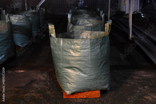 Several sturdy green fabric garden bags containing soil are positioned on orange bricks next to a metal construction frame, illuminated by warm artificial light in an outdoor yard area.