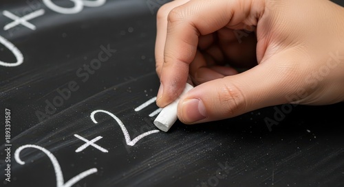 Person writing basic arithmetic operation on a dark slate surface with white chalk