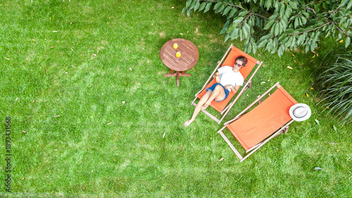 Bild auf Leinwand Young girl relaxes and reading book in summer garden in sunbed deckchair on gras