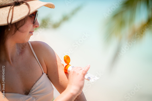 woman applies sunscreen on her arm at beach, wearing straw hat and white top, in serene outdoor setting, promoting sun protection, summer wellness, leisure., Health, Care, Outdoors, Relaxation