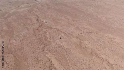 High altitude drone footage showing an isolated vehicle crossing vast arid desert terrain revealing natural tracks scale solitude and the immensity of the landscape
