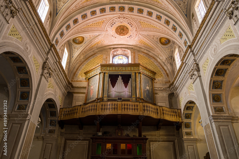 Obraz premium Elaborate wooden pipe organ and decorated balcony inside the Cattedrale dell'Immacolata Concezione in Bosa, Sardinia. Warm daylight streams through arched windows, highlighting intricate architectural