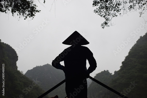 Silhouette of a woman wearing a Vietnamese hat while sailing a boat