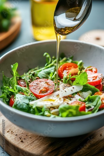 Fresh green salad with cherry tomatoes and cheese being drizzled with olive oil in a bowl.