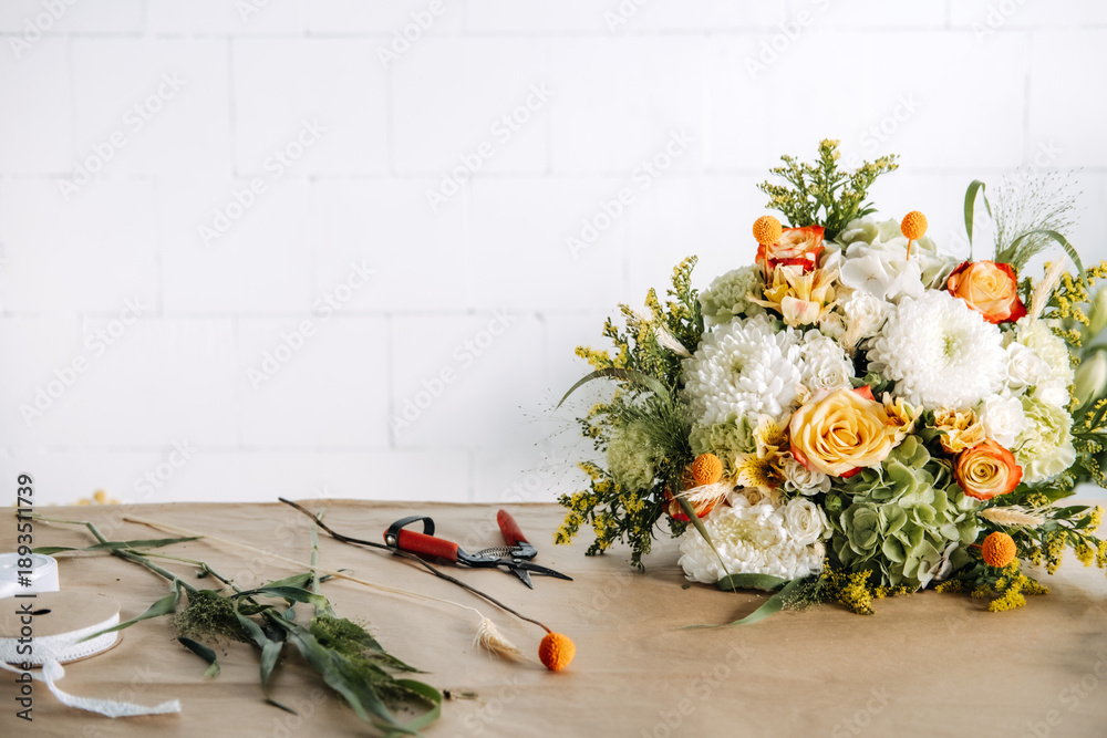 Naklejka premium Large flower arrangement rests on florist workbench near garden shears and ribbons. Boutique florist, local business owner, craft economy, handmade floral arrangements.