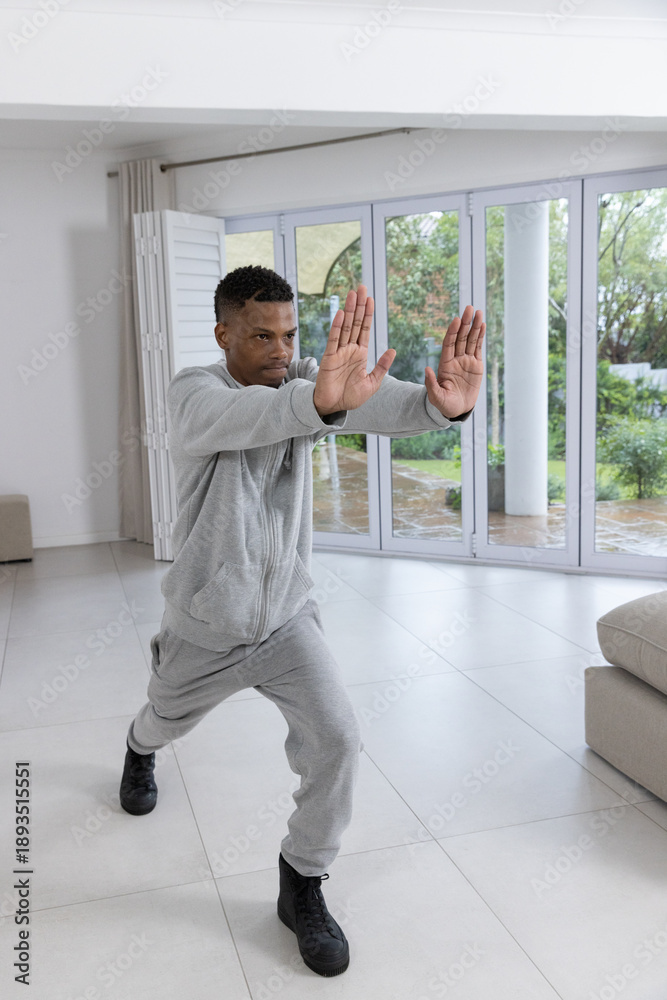 Fototapeta premium African american man practicing martial stance in living room by glass doors
